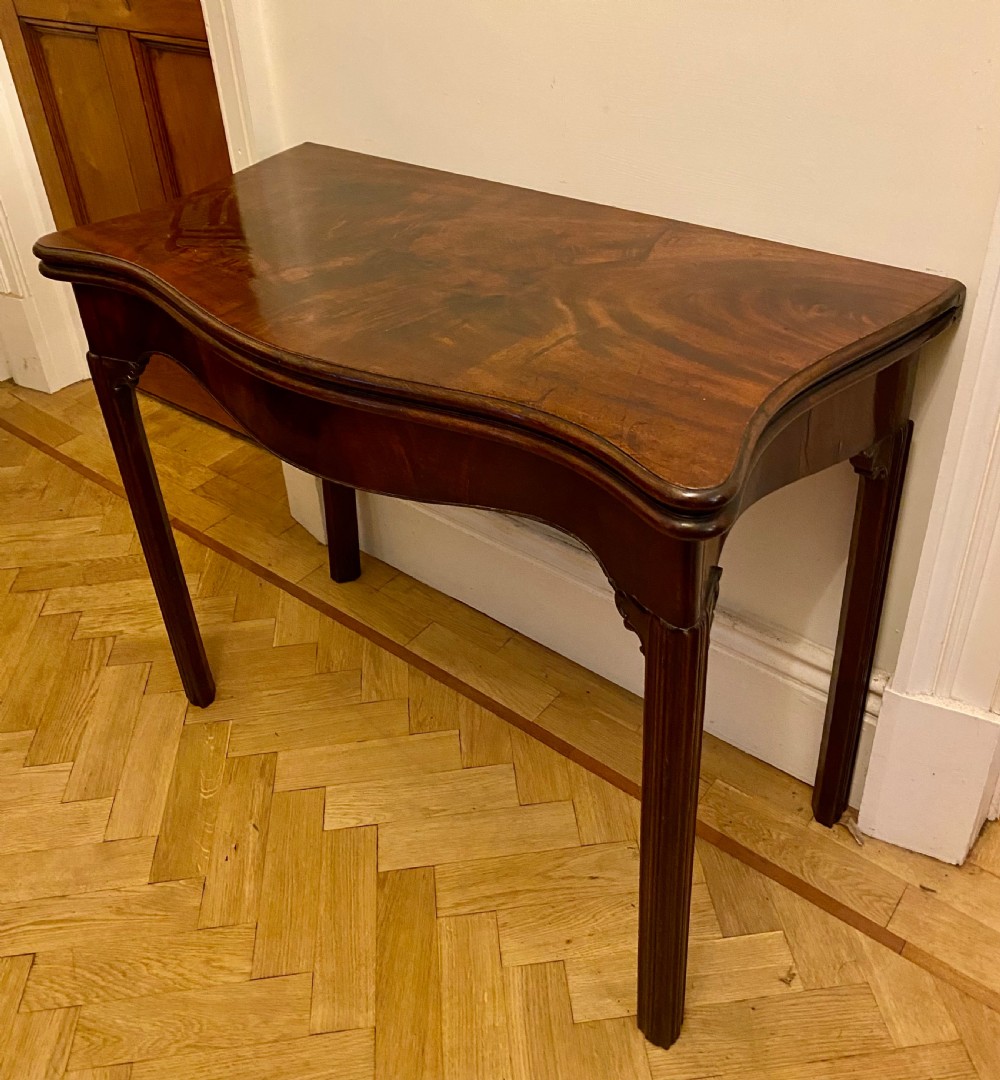 A Georgian mahogany fold-over card table featuring a serpentine front, flame mahogany top veneer, and moulded legs. View VI