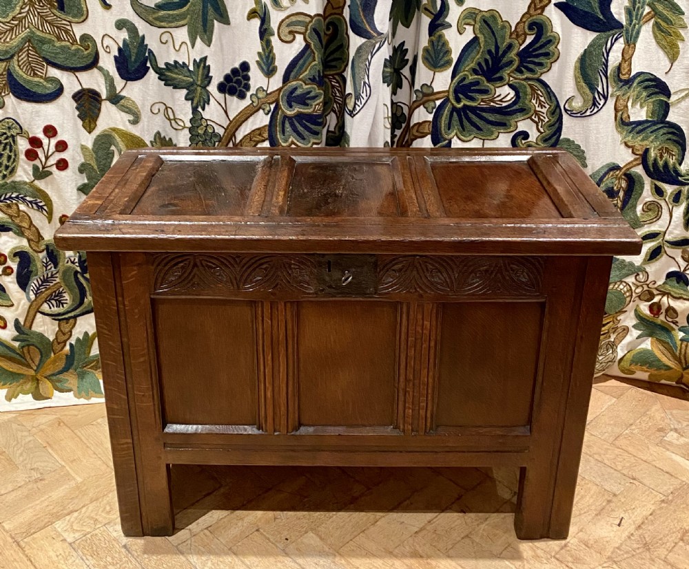 An antique dark oak coffer featuring three carved front panels, a hinged panelled lid, and raised stile legs. View II