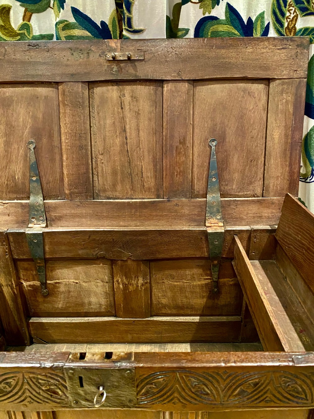 An antique dark oak coffer featuring three carved front panels, a hinged panelled lid, and raised stile legs. View V