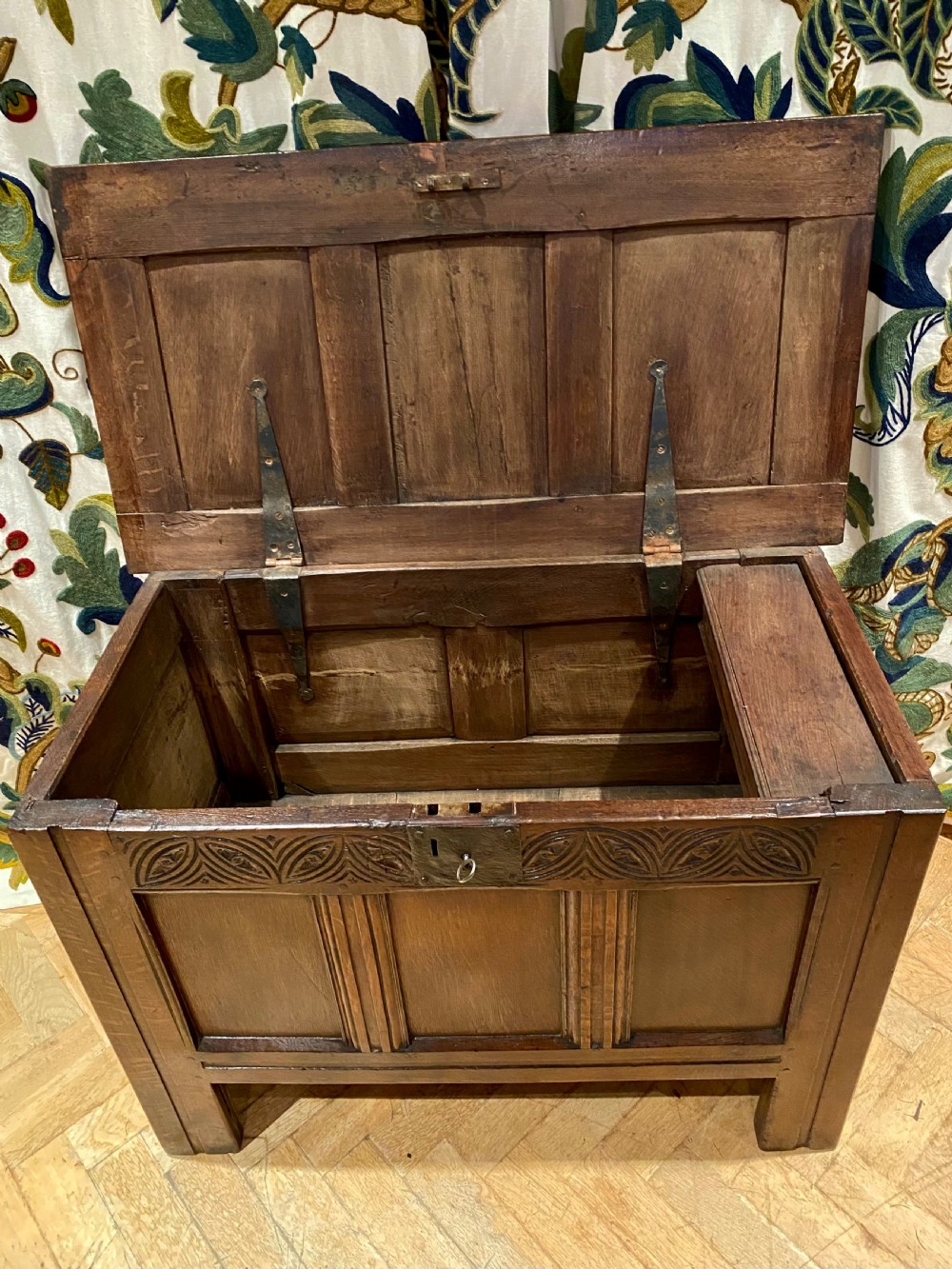 An antique dark oak coffer featuring three carved front panels, a hinged panelled lid, and raised stile legs. View VI