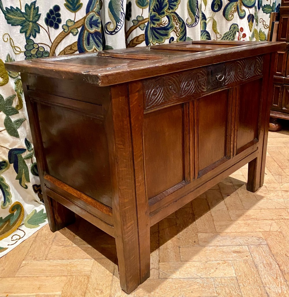 An antique dark oak coffer featuring three carved front panels, a hinged panelled lid, and raised stile legs. View VII