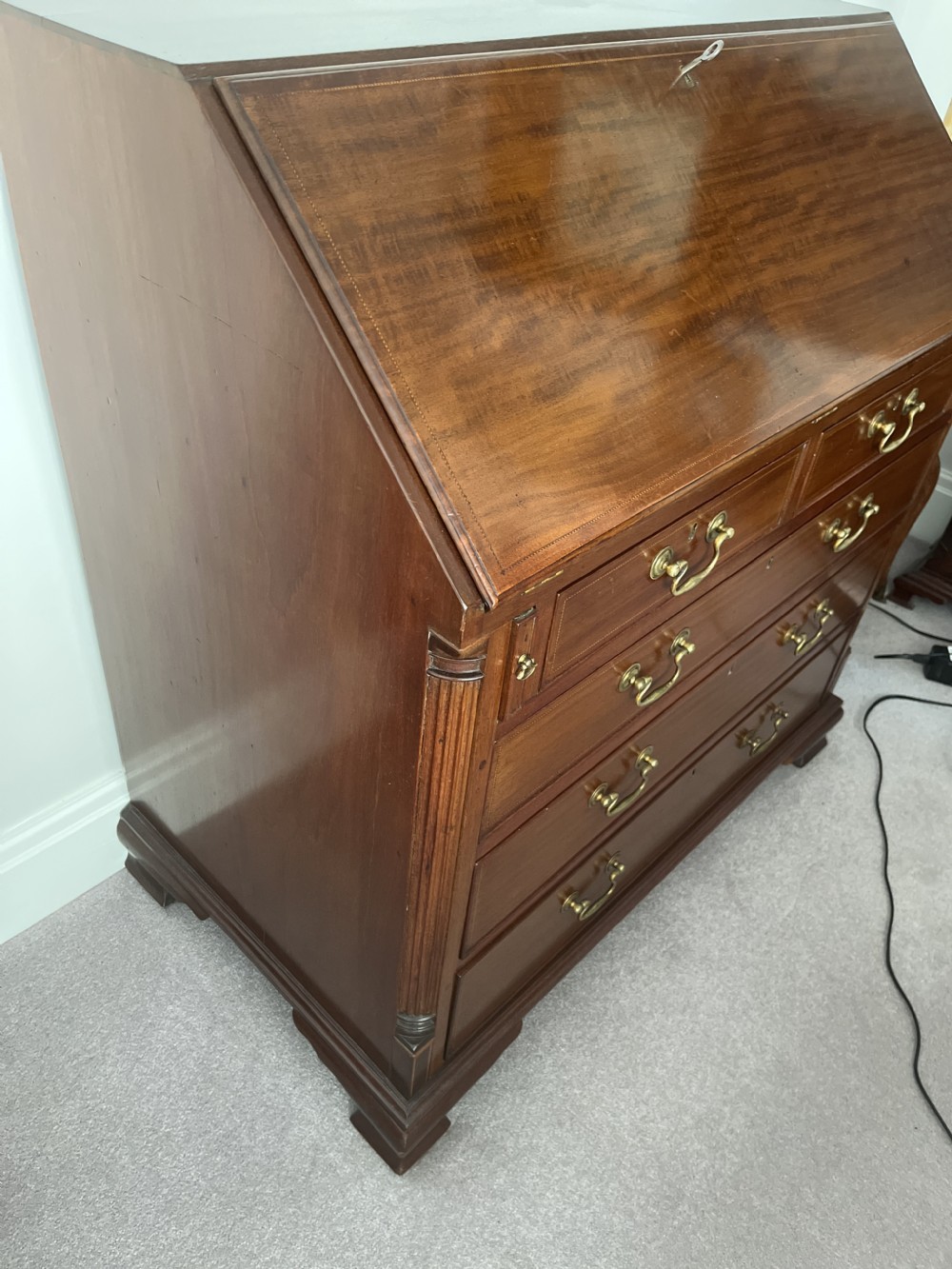 A Georgian mahogany writing bureau featuring a sloped hinged lid above four graduating drawers with brass swan-neck handles. View V