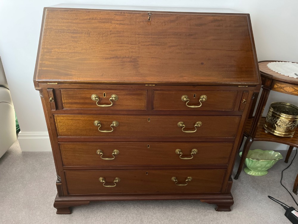 A Georgian mahogany writing bureau featuring a sloped hinged lid above four graduating drawers with brass swan-neck handles.