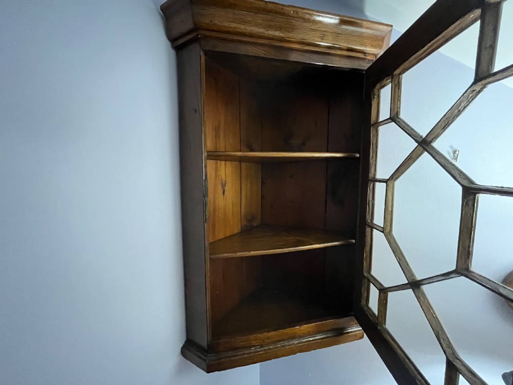 A wall-hanging Georgian oak corner cupboard featuring a single door with geometric astragal glazing and a brass escutcheon. View II