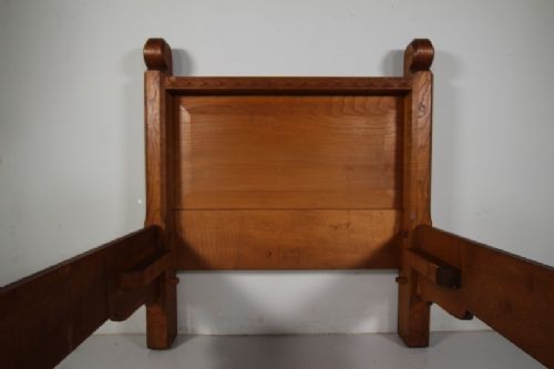 A 1930s solid oak single bed frame featuring carved geometric detailing, panelled headboard and footboard, and sturdy corner posts. View VI