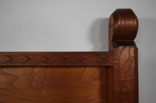A 1930s solid oak single bed frame featuring carved geometric detailing, panelled headboard and footboard, and sturdy corner posts. View VIII