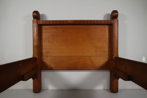 An Arts and Crafts solid chestnut single bed frame featuring carved geometric friezes along the panels and stout square corner posts with scroll finials. View II