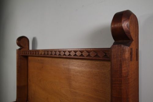 An Arts and Crafts solid chestnut single bed frame featuring carved geometric friezes along the panels and stout square corner posts with scroll finials. View IV