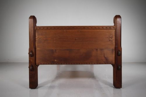An Arts and Crafts solid chestnut single bed frame featuring carved geometric friezes along the panels and stout square corner posts with scroll finials. View V