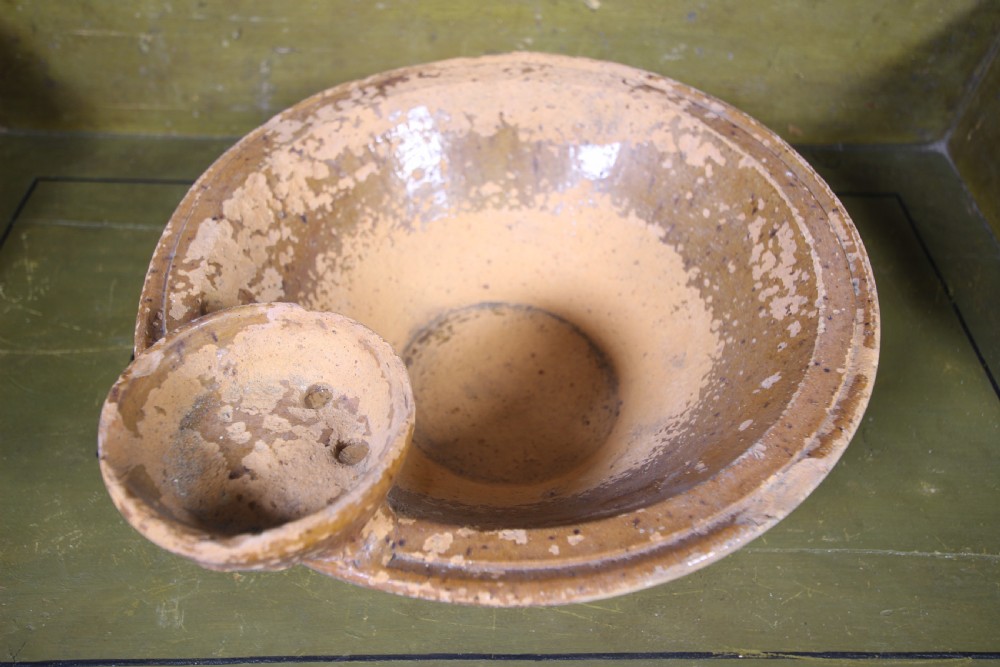 A 19th-century earthenware wash bowl featuring a weathered honey-coloured glaze and an integrated soap dish attached to the rim.
