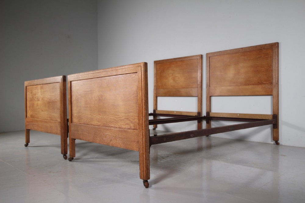 A pair of matching antique Arts and Crafts oak single bed frames with panelled headboards and footboards on castors.