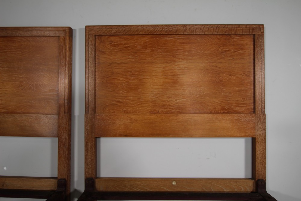 A pair of matching antique Arts and Crafts oak single bed frames with panelled headboards and footboards on castors. View III