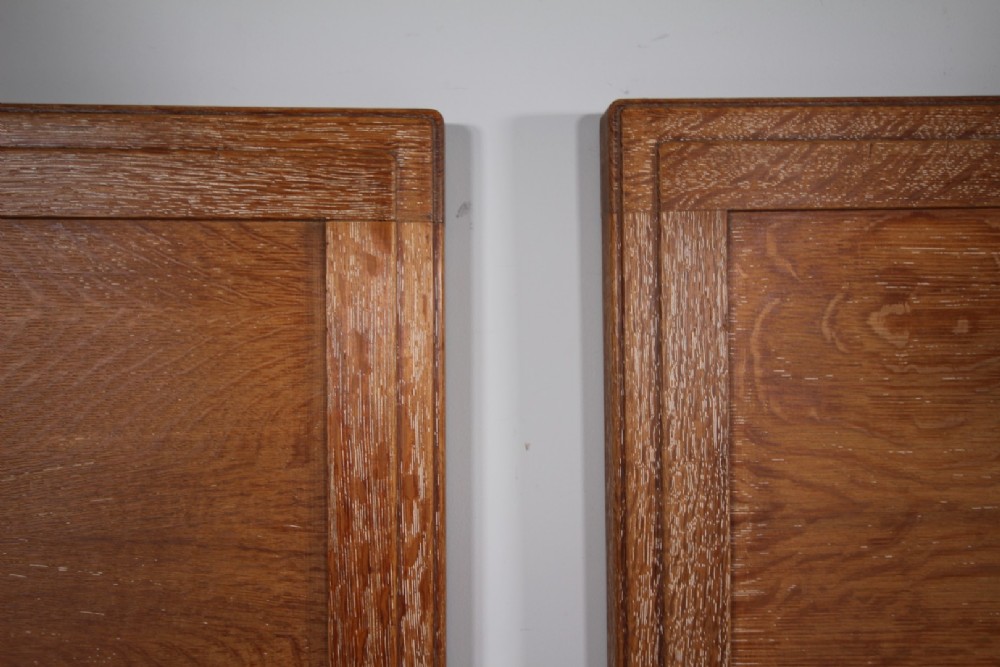A pair of matching antique Arts and Crafts oak single bed frames with panelled headboards and footboards on castors. View IV