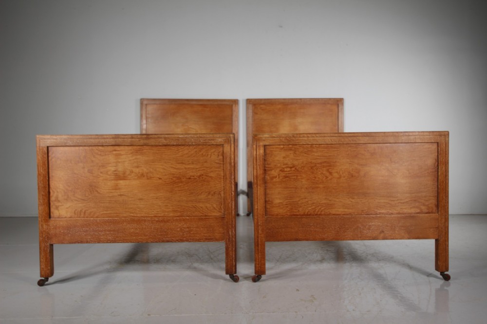A pair of matching antique Arts and Crafts oak single bed frames with panelled headboards and footboards on castors. View V