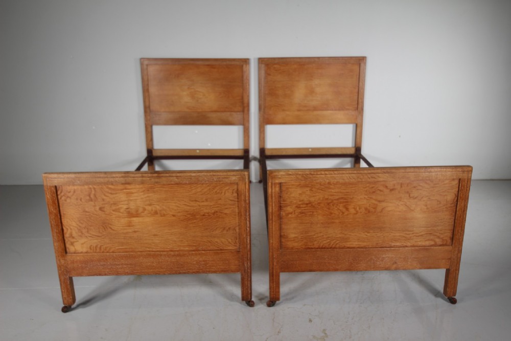 A pair of matching antique Arts and Crafts oak single bed frames with panelled headboards and footboards on castors. View VIII