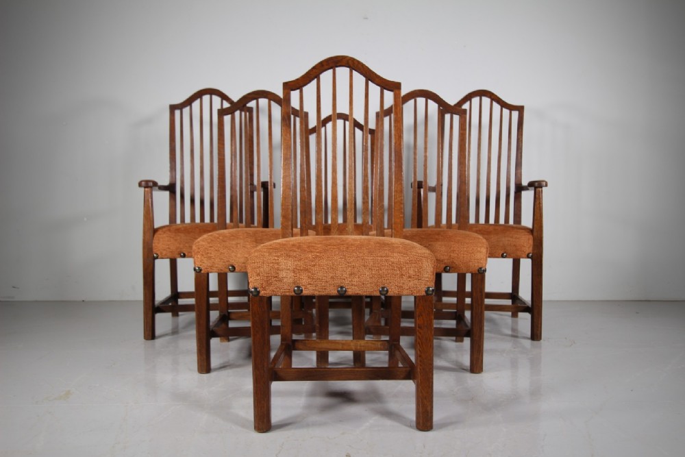 Set of six solid oak Arts and Crafts dining chairs featuring tall spindled backs and terracotta fabric upholstered seats.
