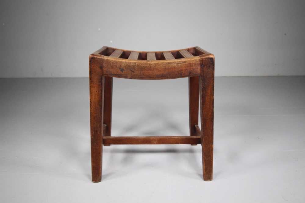 An English Georgian mahogany stool featuring a concave slatted seat, square tapered legs, and a low H-stretcher frame. View V