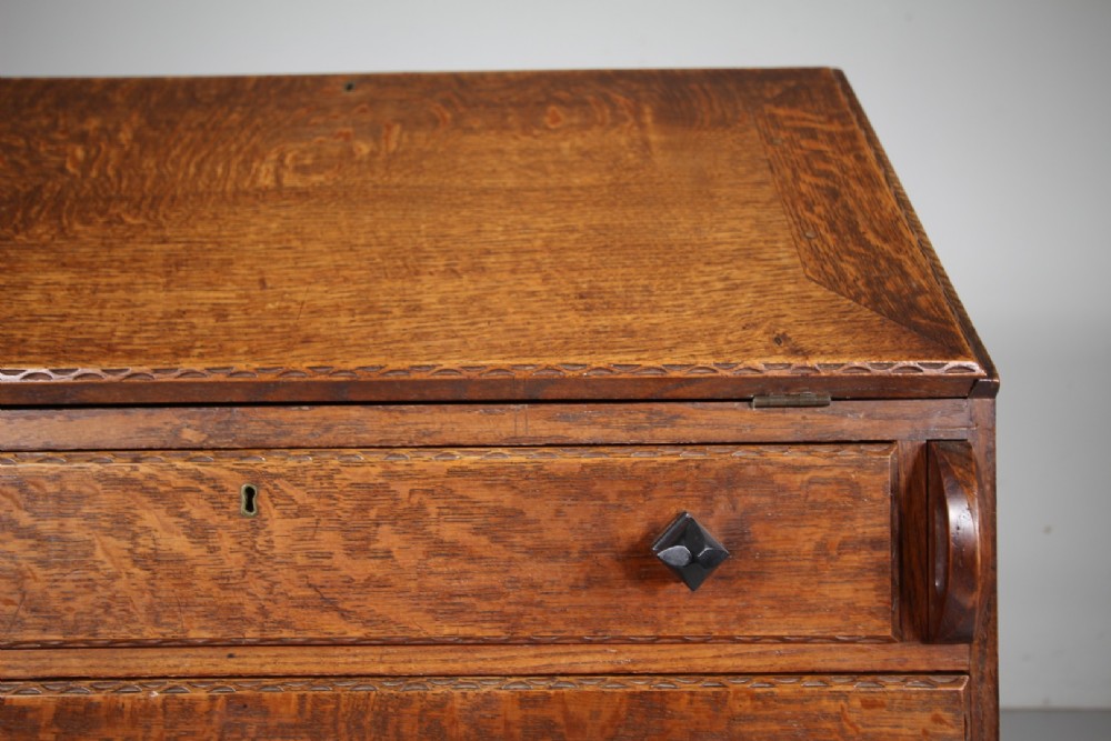 A 1930s oak writing bureau featuring a sloping fall-front lid over two drawers, supported by square legs with an H-stretcher. View X