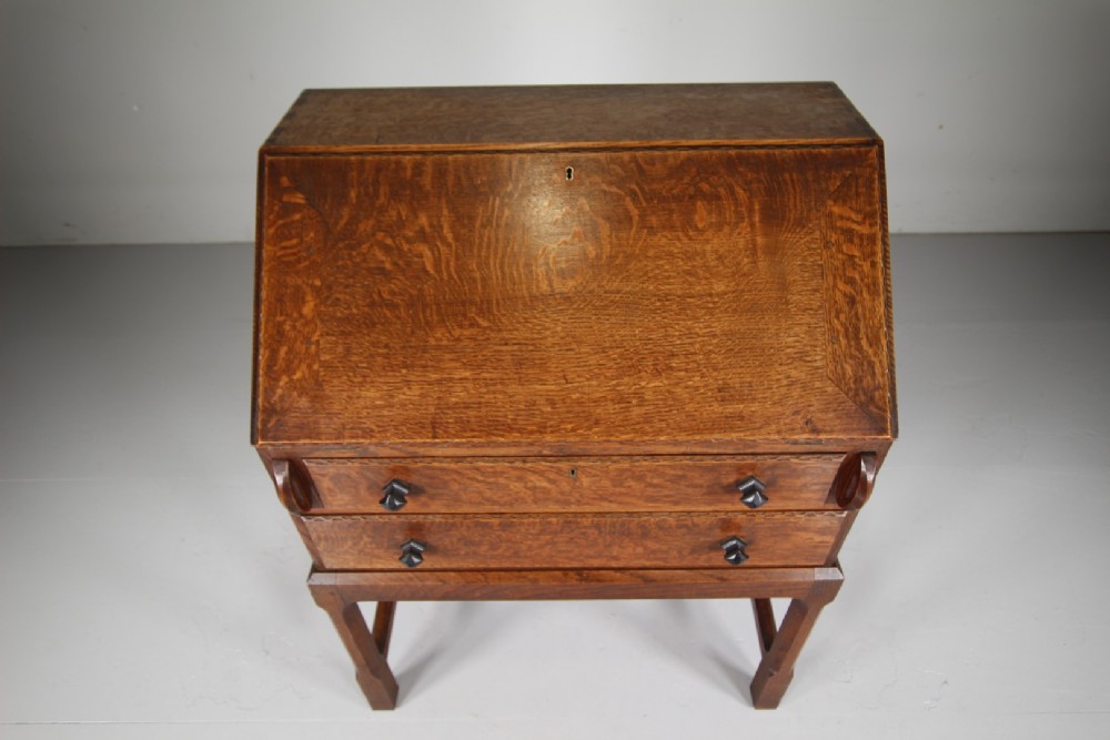 A 1930s oak writing bureau featuring a sloping fall-front lid over two drawers, supported by square legs with an H-stretcher. View XI