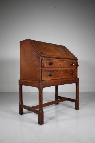 A 1930s oak writing bureau featuring a sloping fall-front lid over two drawers, supported by square legs with an H-stretcher.