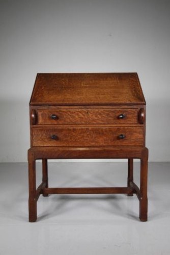 A 1930s oak writing bureau featuring a sloping fall-front lid over two drawers, supported by square legs with an H-stretcher. View IX