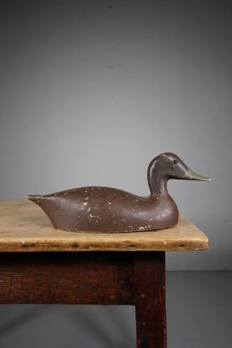 A 19th-century carved wooden decoy duck with a dark brown painted finish shown in profile. View II
