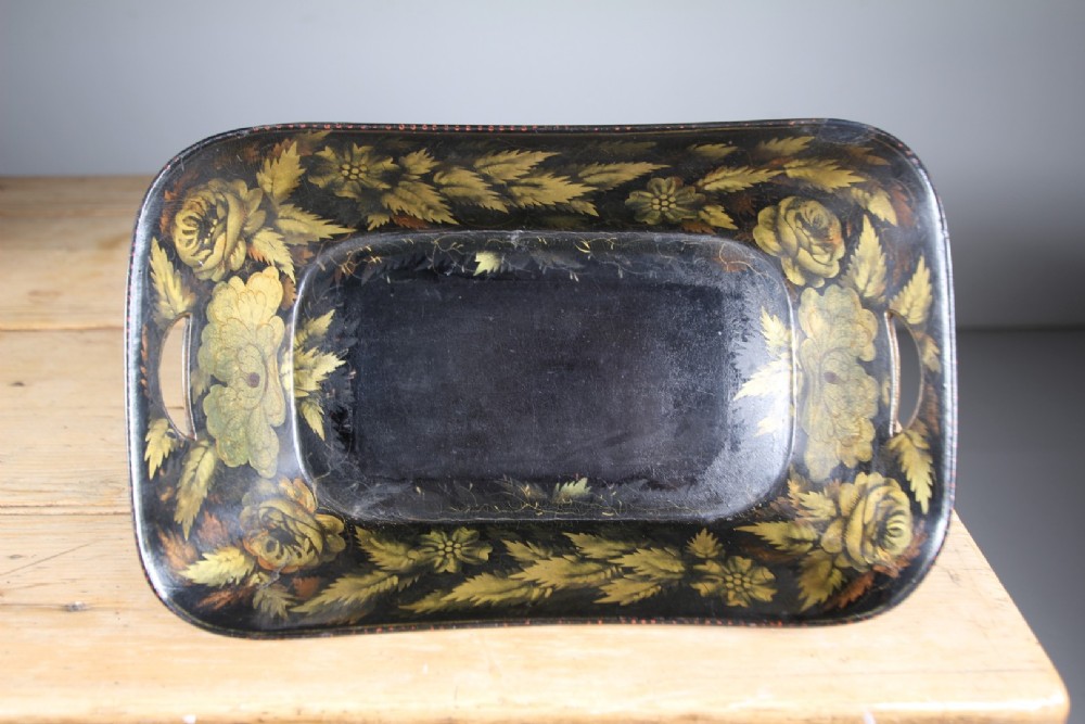 An antique black lacquered papier-mache tray featuring hand-painted gold floral borders and integrated side handles.