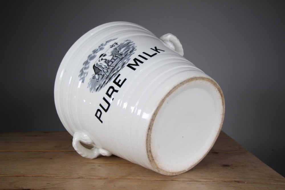 A white glazed ironstone dairy pail featuring integrated side handles, horizontal ribbed detailing, and a black transferware illustration of cows above the text PURE MILK. View IV