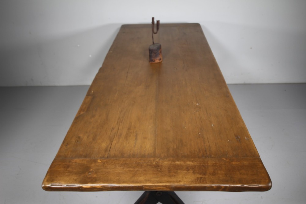A 19th-century oak tavern dining table featuring a natural timber top, a black painted X-frame trestle base, and a central iron stretcher. View V