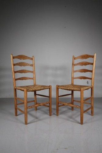A pair of 1920s Arts and Crafts oak side chairs with ladderback frames and woven rush seats.