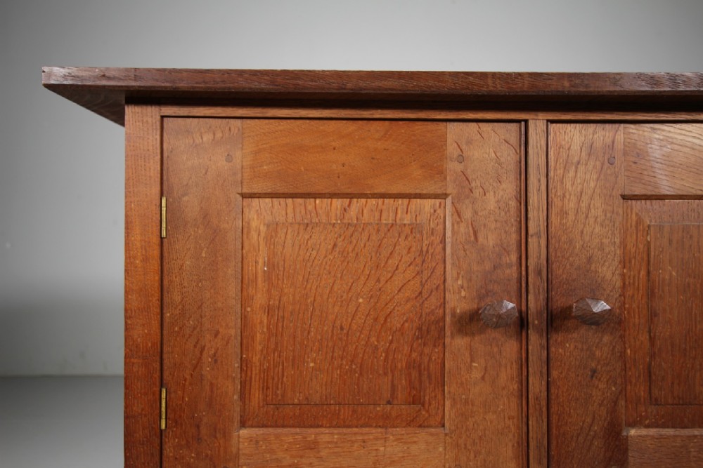 A solid oak two-door cupboard featuring recessed square door panels, carved wooden handles, and four square straight legs. View V