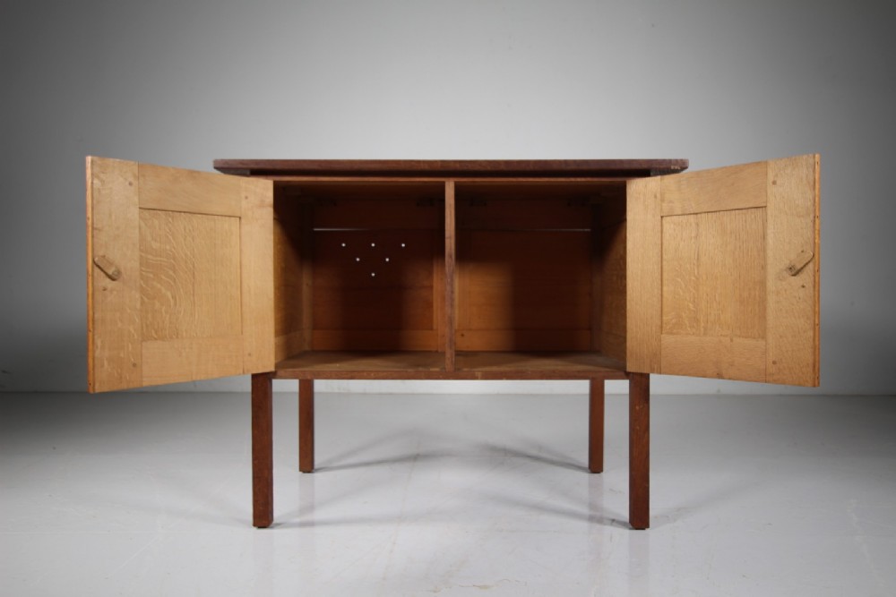 A solid oak two-door cupboard featuring recessed square door panels, carved wooden handles, and four square straight legs. View VI