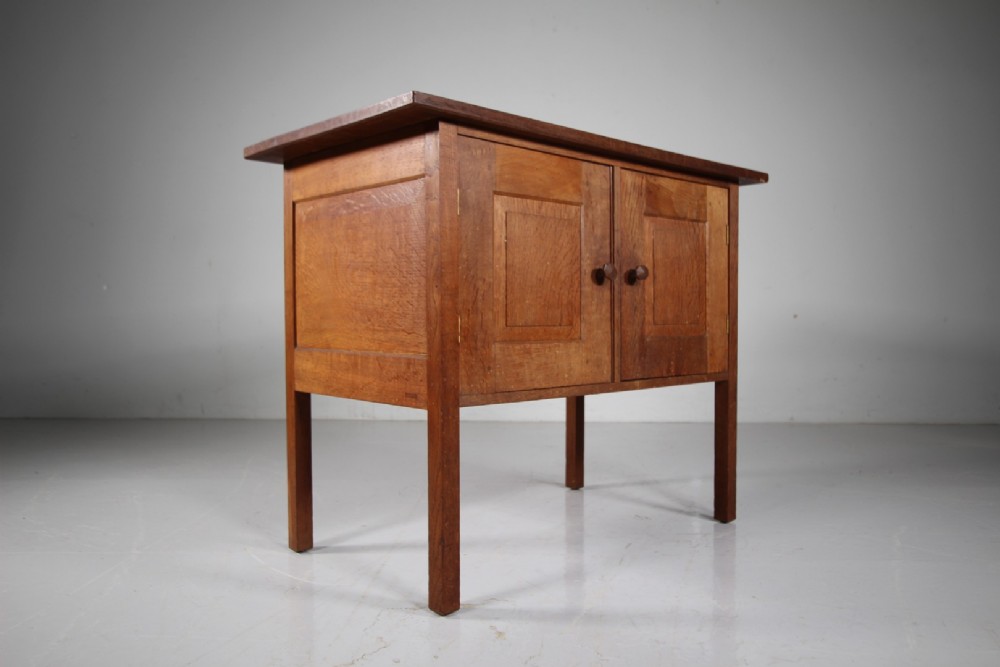 A solid oak two-door cupboard featuring recessed square door panels, carved wooden handles, and four square straight legs. View IX
