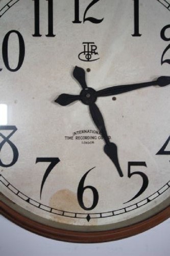 A circular antique Edwardian wall clock featuring a copper bezel, off-white dial with black Arabic numerals, and stylized spade hands. View III