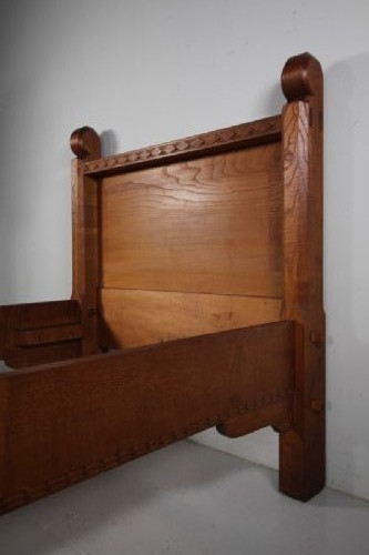 A 1930s solid oak single bed frame featuring carved geometric detailing, panelled headboard and footboard, and sturdy corner posts. View II