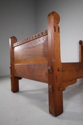 A 1930s solid oak single bed frame featuring carved geometric detailing, panelled headboard and footboard, and sturdy corner posts. View IV