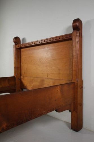 An Arts and Crafts solid chestnut single bed frame featuring carved geometric friezes along the panels and stout square corner posts with scroll finials. View III