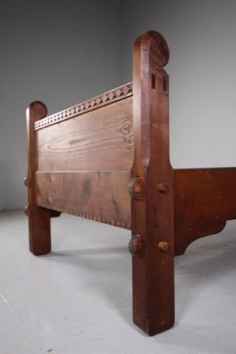 An Arts and Crafts solid chestnut single bed frame featuring carved geometric friezes along the panels and stout square corner posts with scroll finials. View VII