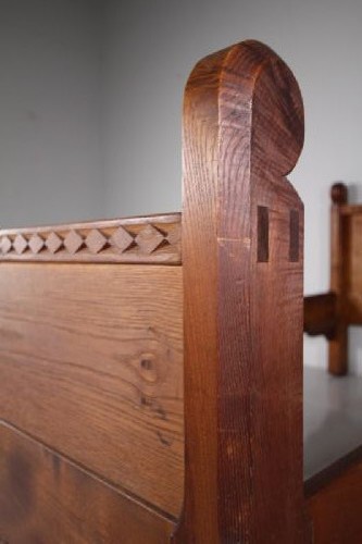 An Arts and Crafts solid chestnut single bed frame featuring carved geometric friezes along the panels and stout square corner posts with scroll finials. View VIII