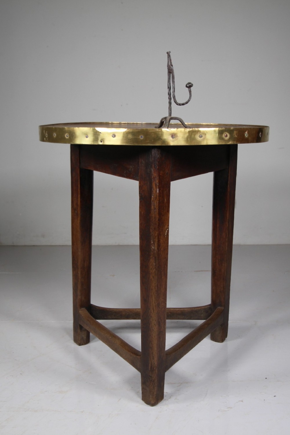 A nineteenth-century dark oak three-legged cricket table featuring a circular top bound with a studded brass rim and supported by a triangular stretcher. View II