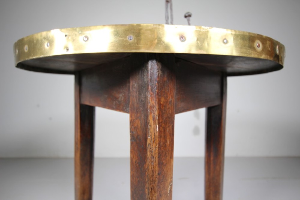 A nineteenth-century dark oak three-legged cricket table featuring a circular top bound with a studded brass rim and supported by a triangular stretcher. View VI