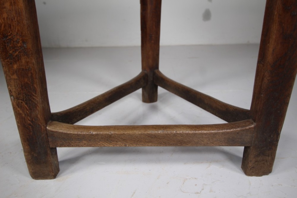 A nineteenth-century dark oak three-legged cricket table featuring a circular top bound with a studded brass rim and supported by a triangular stretcher. View VII