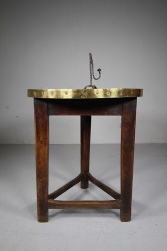 A nineteenth-century dark oak three-legged cricket table featuring a circular top bound with a studded brass rim and supported by a triangular stretcher.
