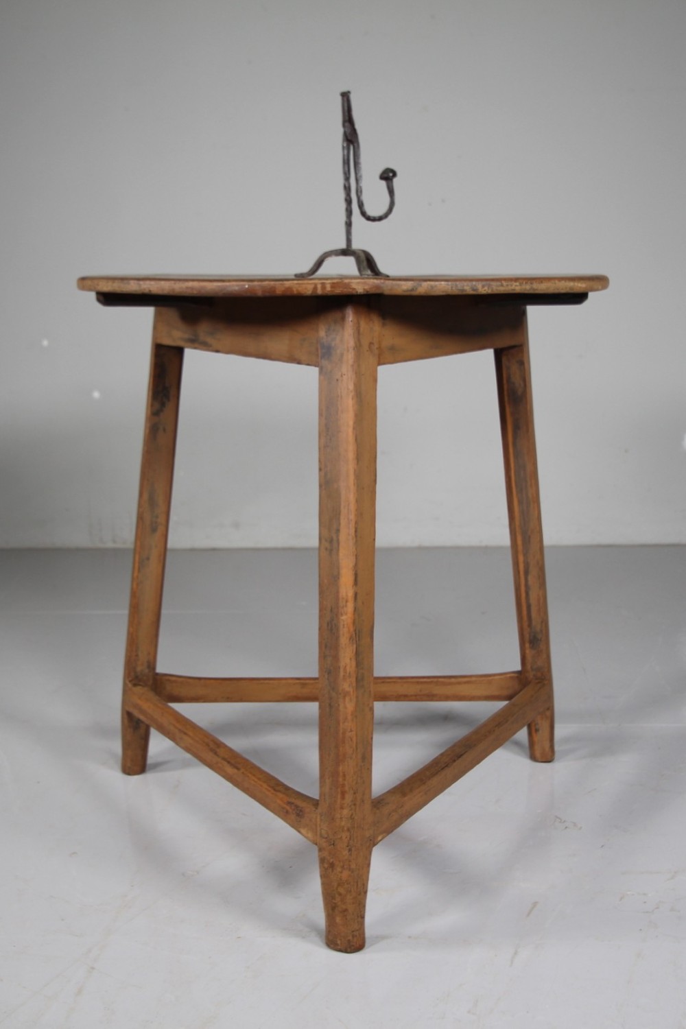 An 18th-century painted pine cricket table featuring a circular wooden top supported by three legs and triangular lower stretchers.