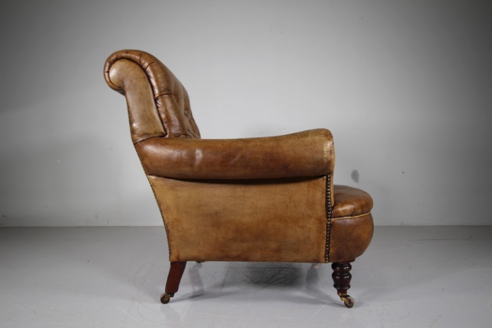 A 19th-century English leather armchair featuring deep-buttoned upholstery in tan brown hide, rolled arms, and turned mahogany front legs with brass castors. View V