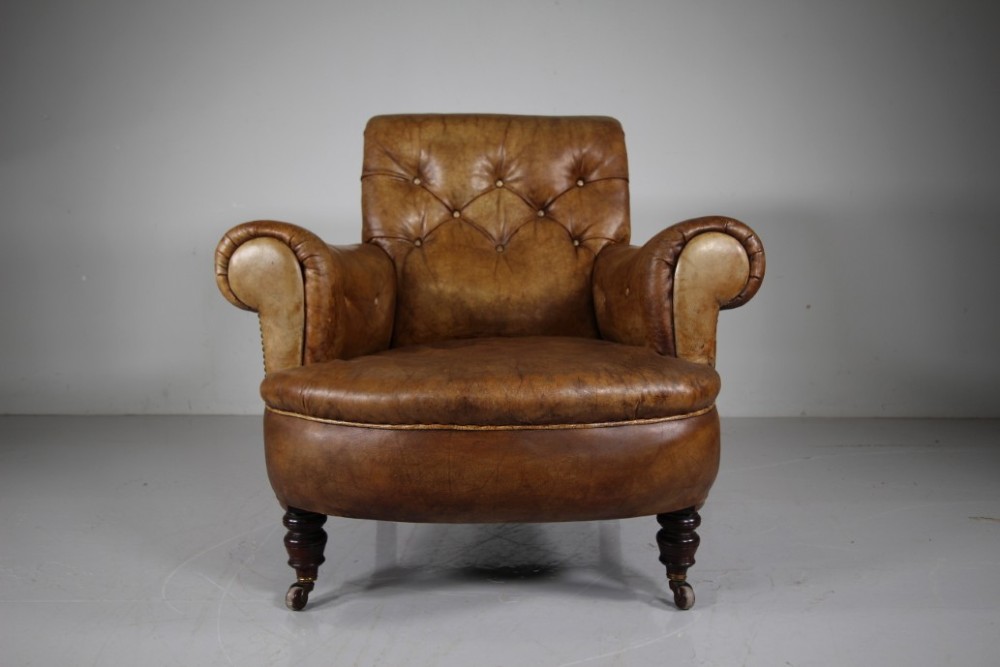 A 19th-century English leather armchair featuring deep-buttoned upholstery in tan brown hide, rolled arms, and turned mahogany front legs with brass castors. View VII