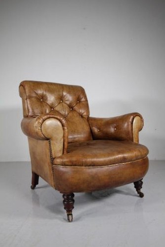 A 19th-century English leather armchair featuring deep-buttoned upholstery in tan brown hide, rolled arms, and turned mahogany front legs with brass castors.