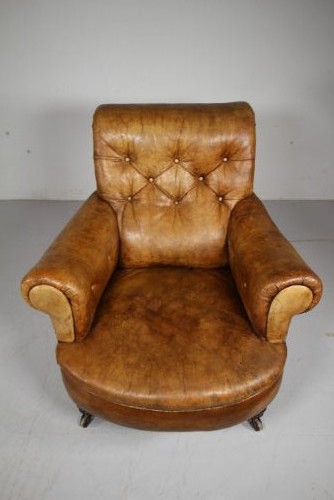 A 19th-century English leather armchair featuring deep-buttoned upholstery in tan brown hide, rolled arms, and turned mahogany front legs with brass castors. View II