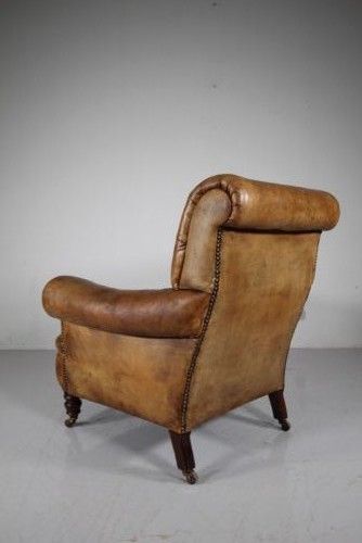 A 19th-century English leather armchair featuring deep-buttoned upholstery in tan brown hide, rolled arms, and turned mahogany front legs with brass castors. View VI