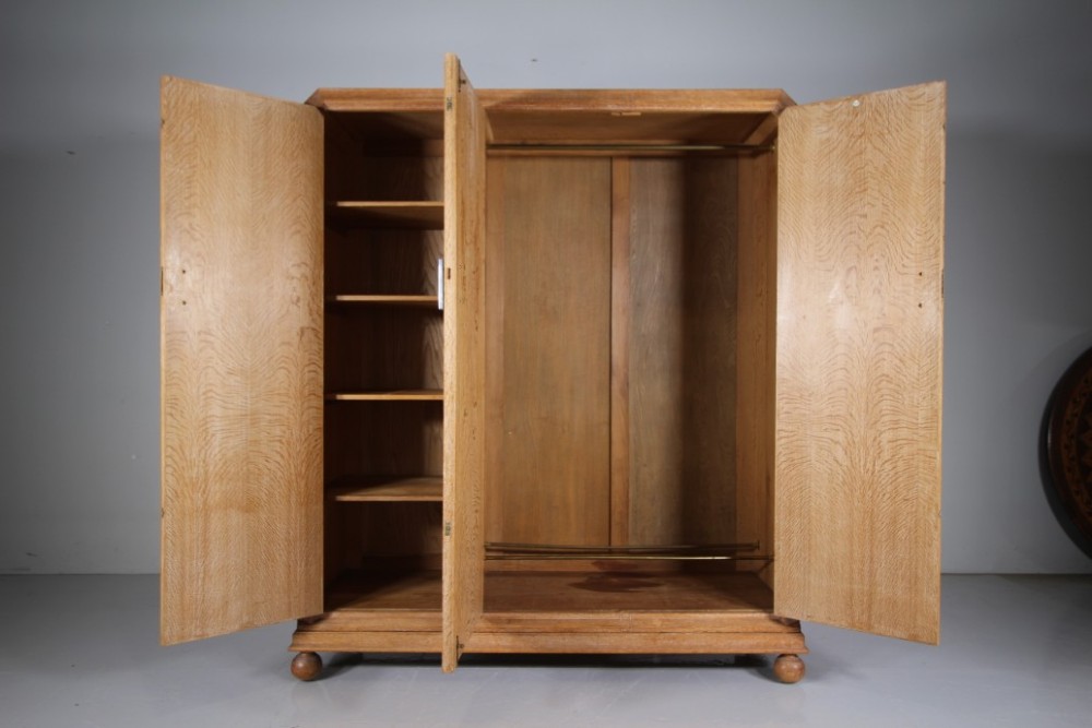 A 1920s Heals solid oak triple-door wardrobe with chamfered top corners, vertical wooden handles, and bun feet. View IV